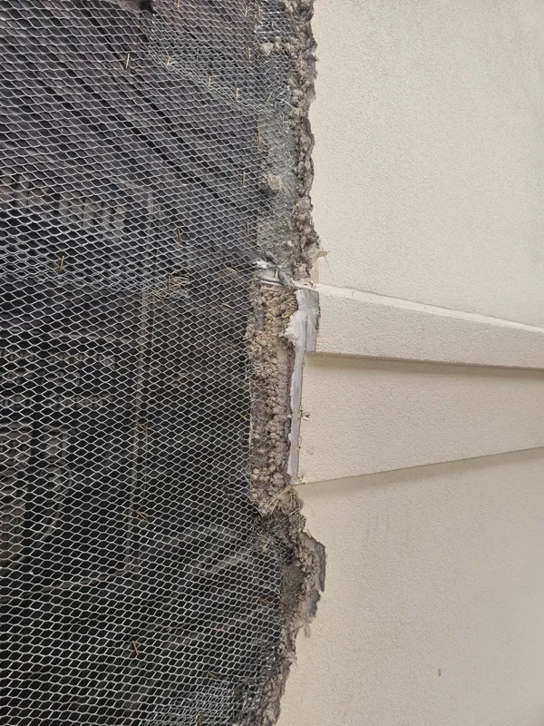 Metal lath and stucco layers visible beside a window