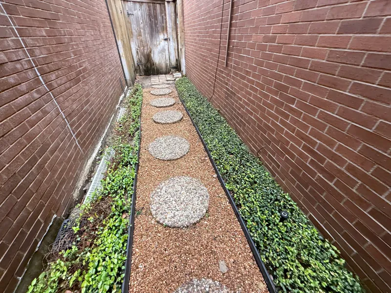 Narrow side passage with stepping stones between brick walls