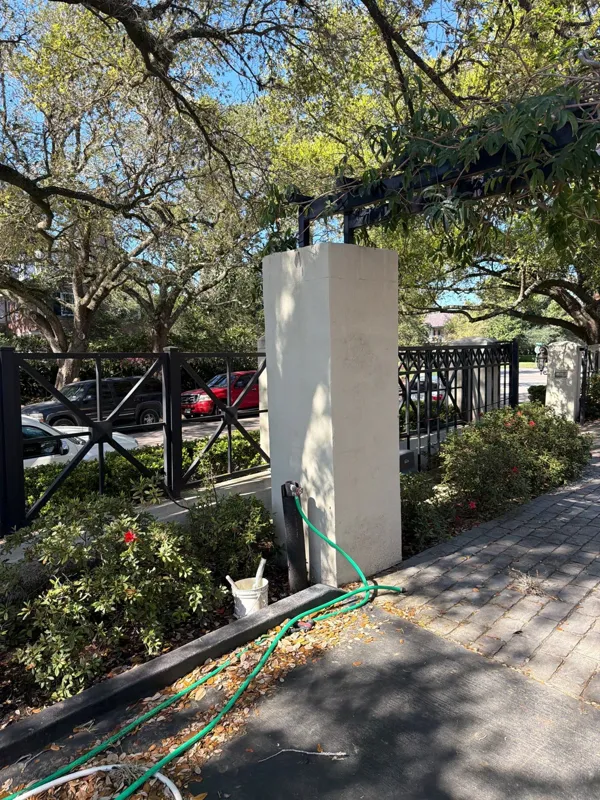 Light-colored exterior column beside trees and a fence