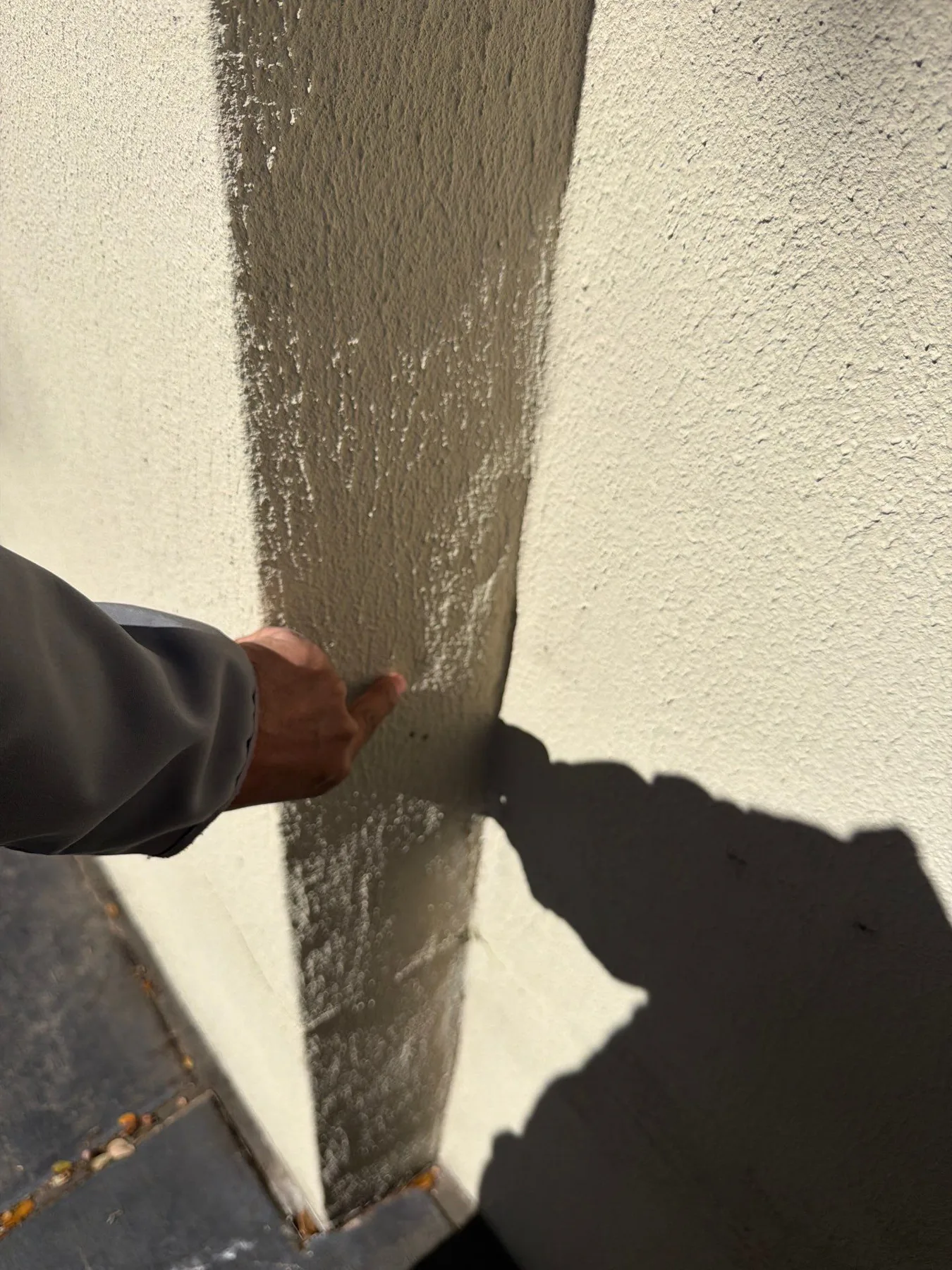 Gloved hand applying a coating at a stucco wall edge